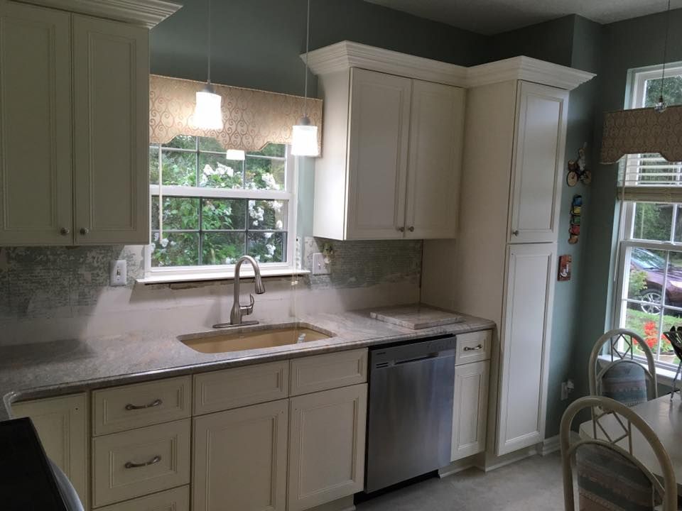 A kitchen with white cabinets , a sink , a dishwasher , and a window.