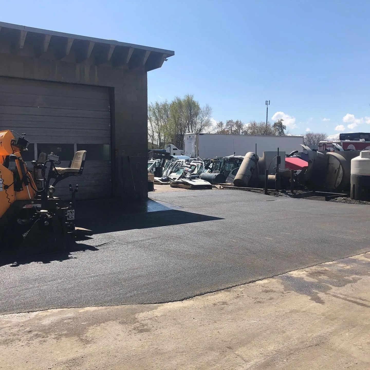 Asphalt parking lot next to a garage with tanks and equipment in the background. Sunny, outdoor setting.