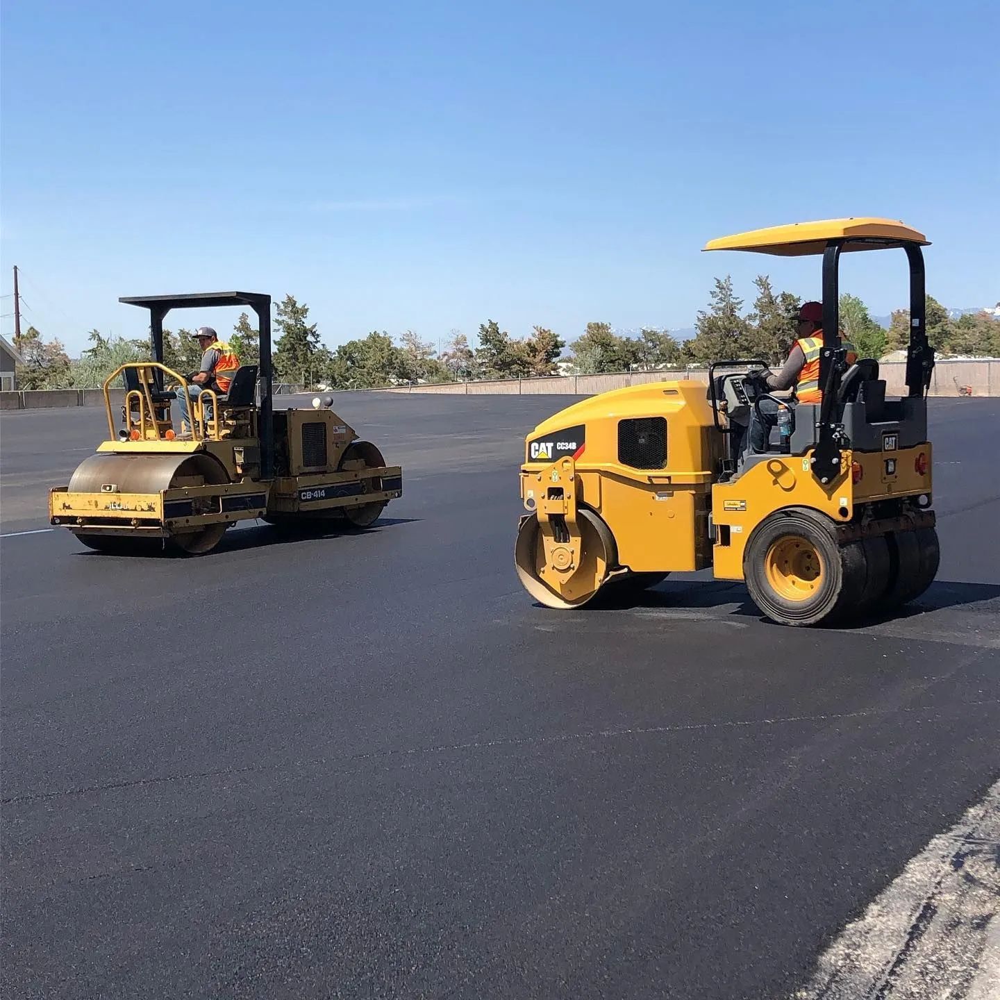 Two yellow road rollers compacting fresh asphalt on a sunny day.