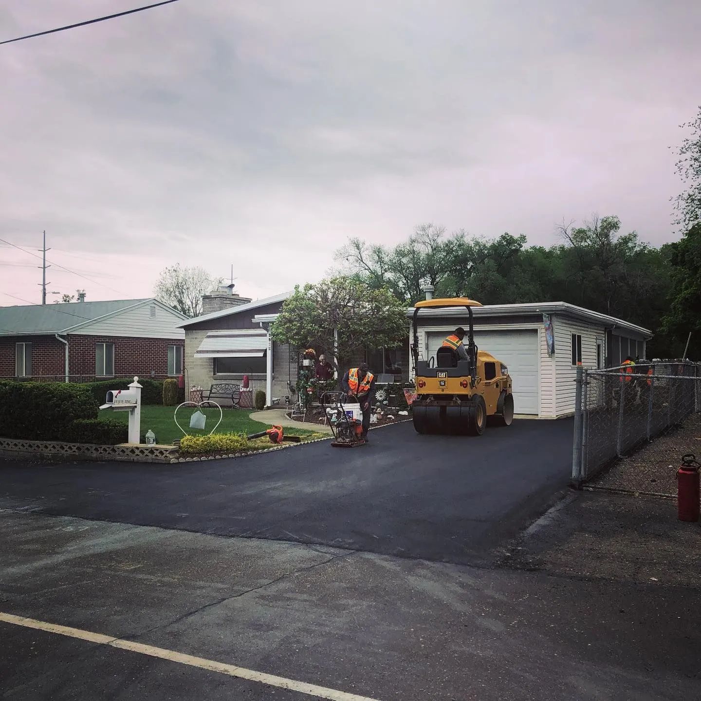 Asphalt paving a residential driveway; roller compacting newly laid asphalt.