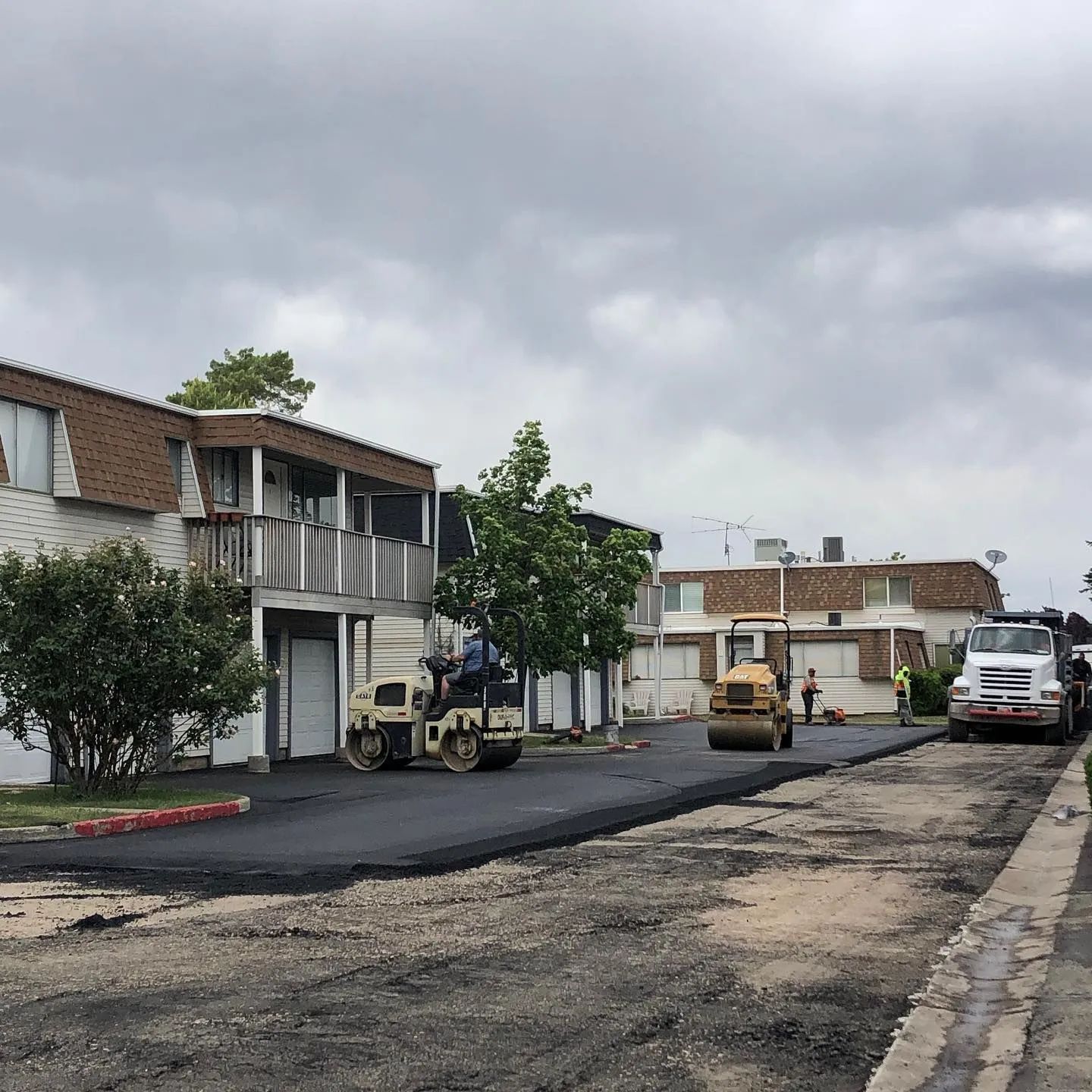 Asphalt paving of a street in front of apartment buildings; workers and equipment present.