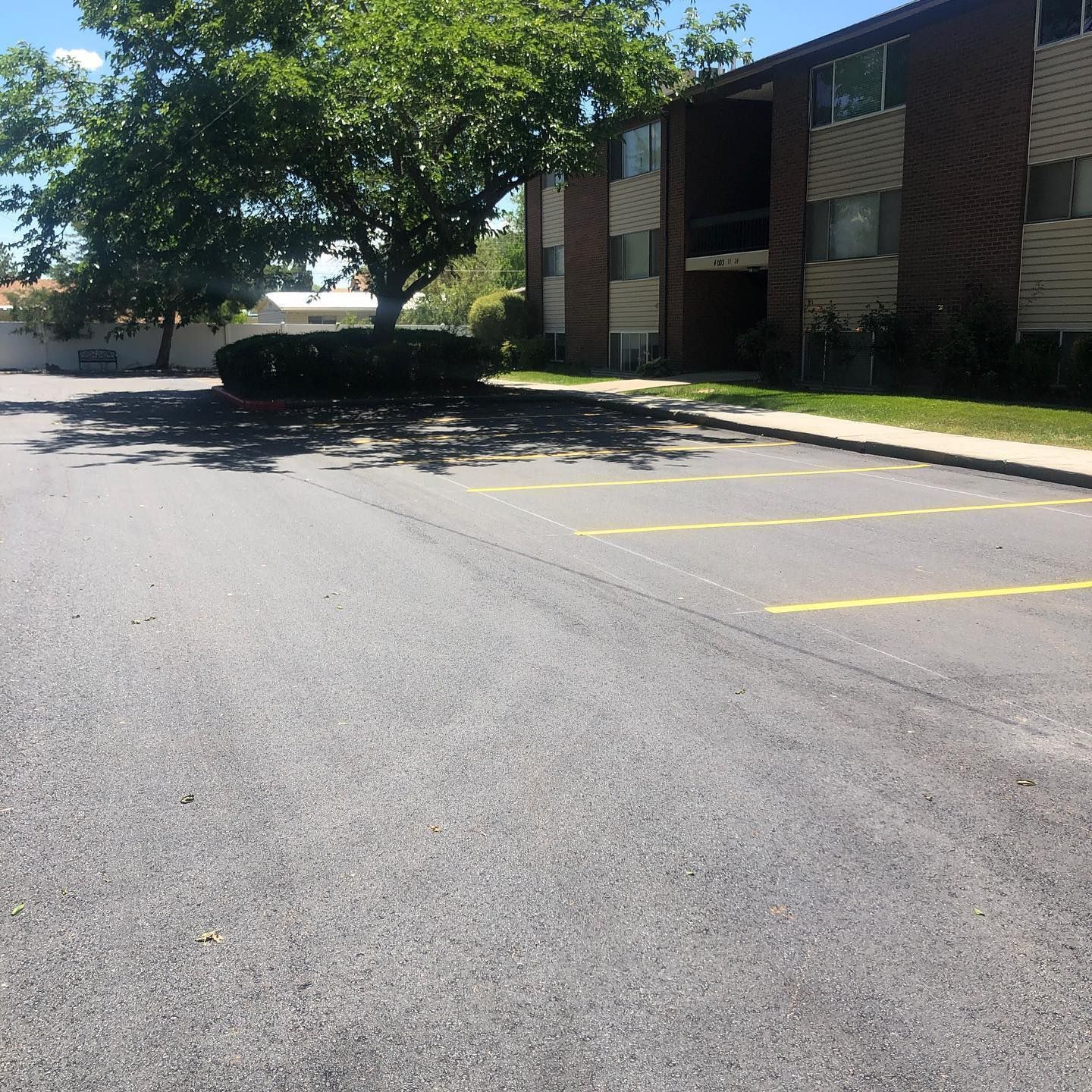 Empty asphalt parking lot in front of a brick apartment building on a sunny day.