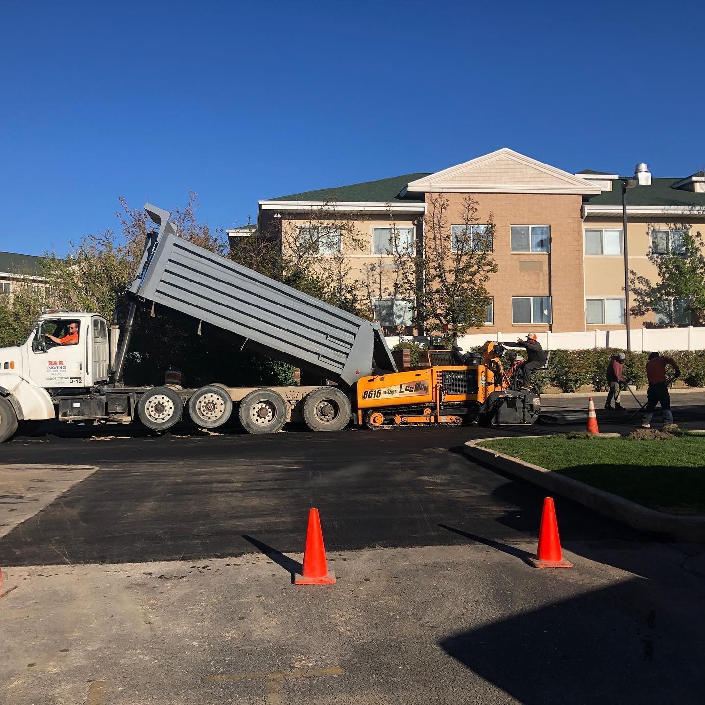 A dump truck unloading asphalt into a paving machine on a road near a building.