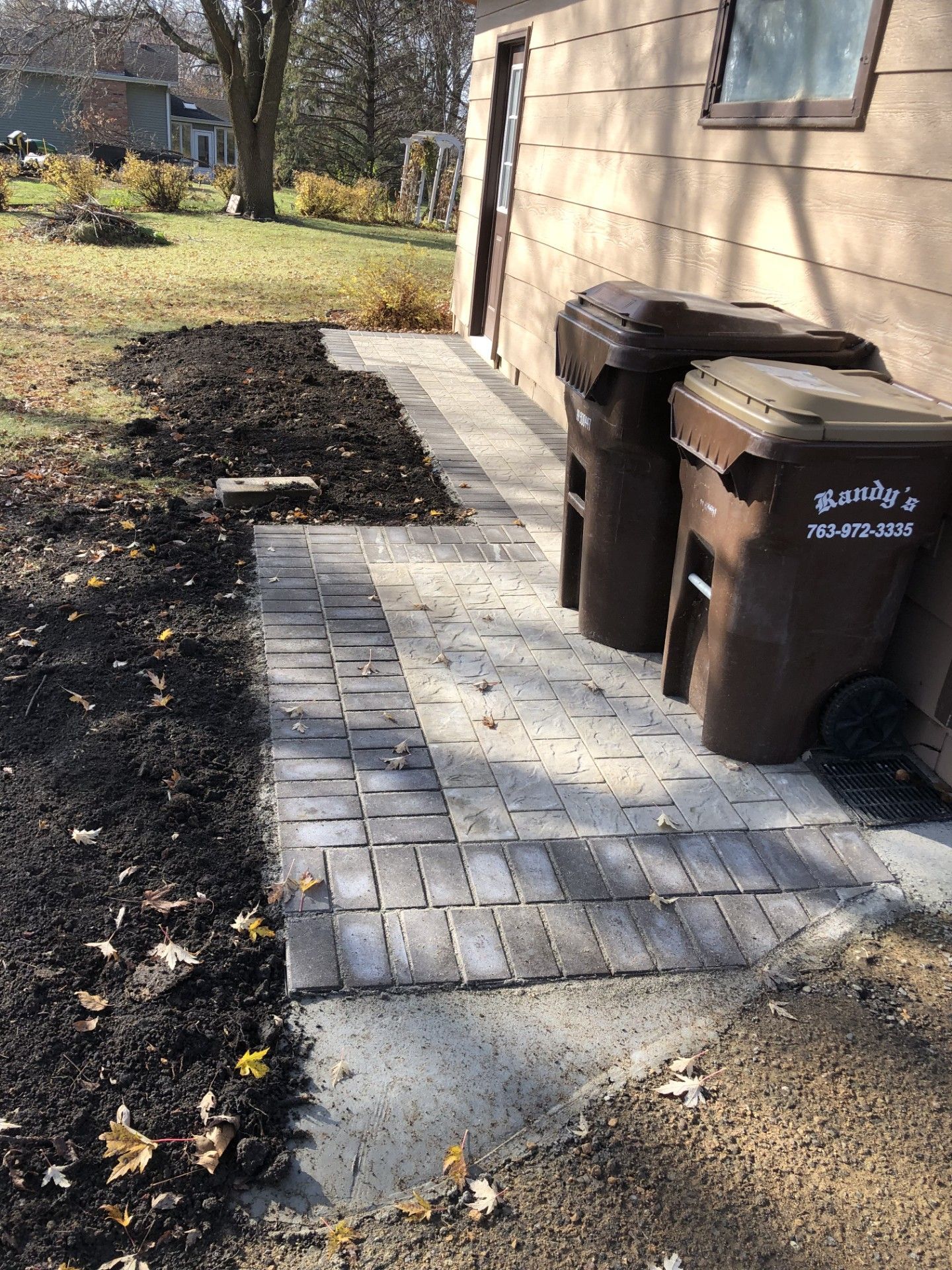 Two trash cans are sitting on a sidewalk next to a house.