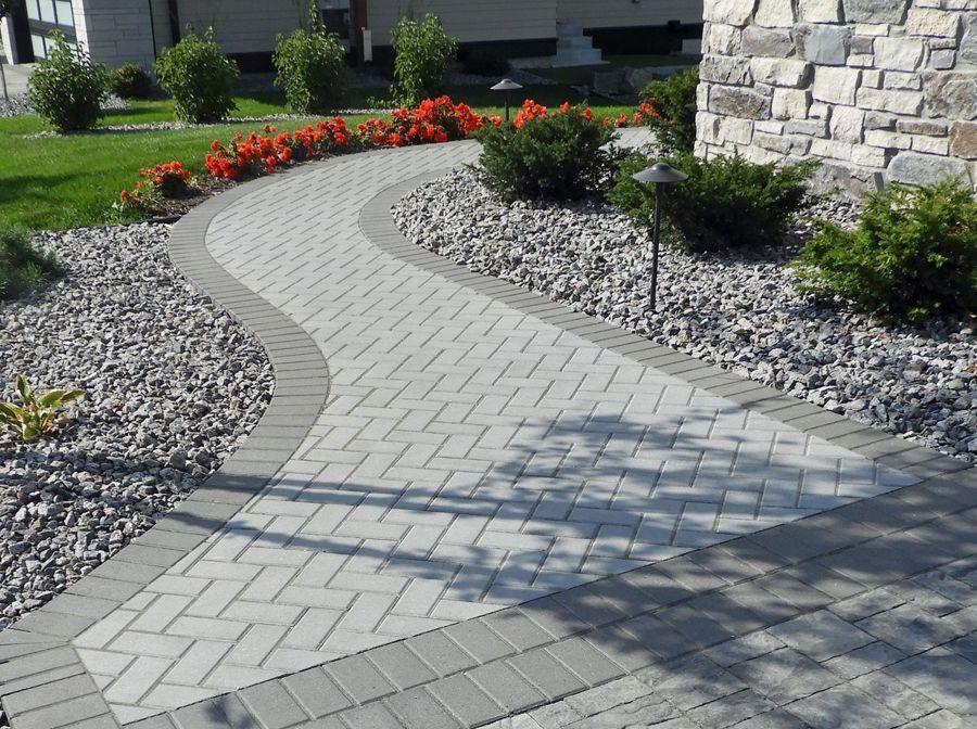 A brick walkway leading to a house with flowers on the side.