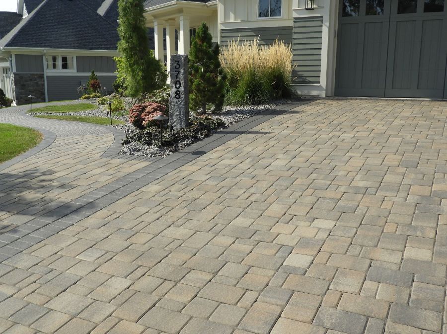 A brick driveway in front of a house with a gray garage door.