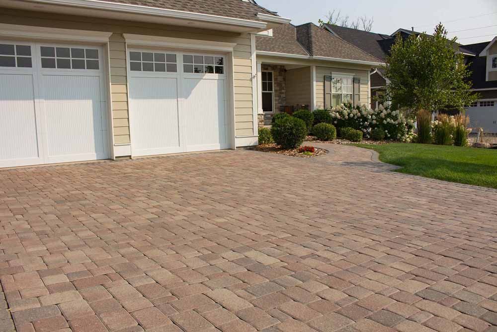 a brick driveway in front of a house with two garage doors