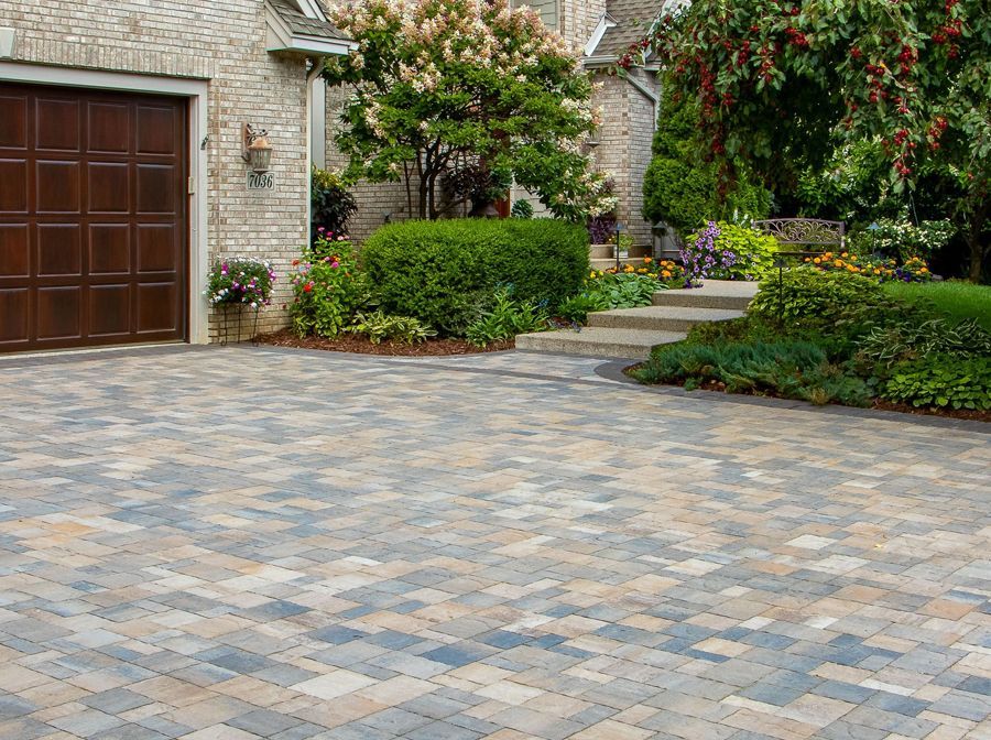 A brick driveway in front of a brick house with a wooden garage door and a lush garden.