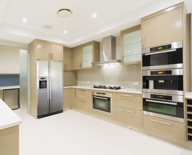 Modern kitchen with light wood cabinets, stainless steel appliances, and white countertops.