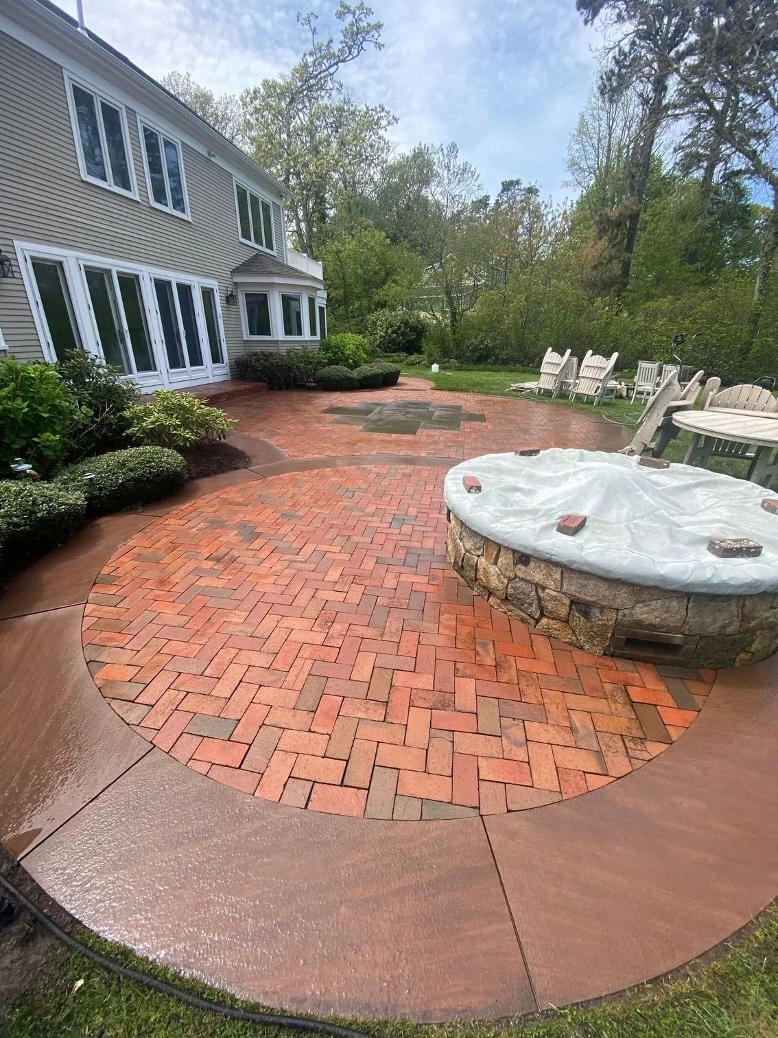 Brick patio with fire pit, surrounded by brown stone and grass, beside a house.