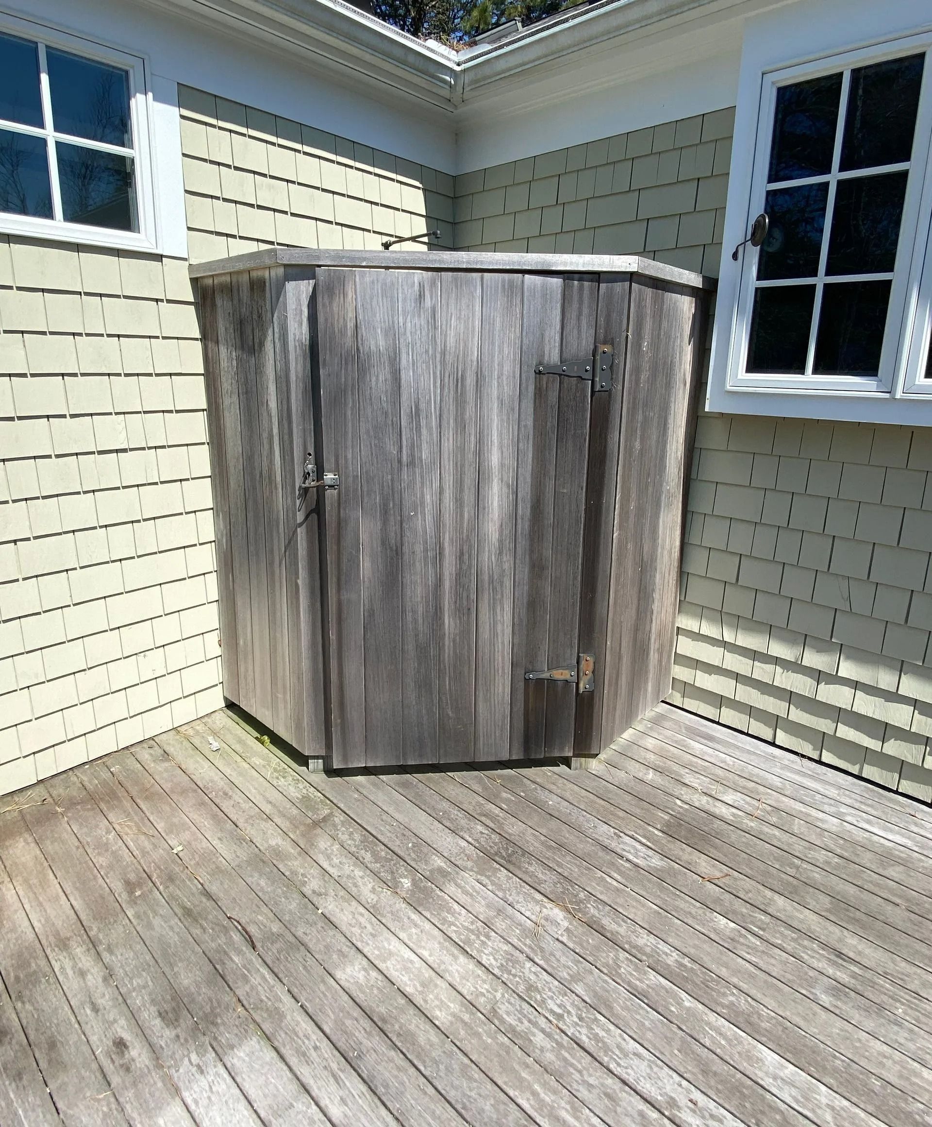 Weathered wooden storage unit on a wooden deck, beside a pale yellow building with windows.