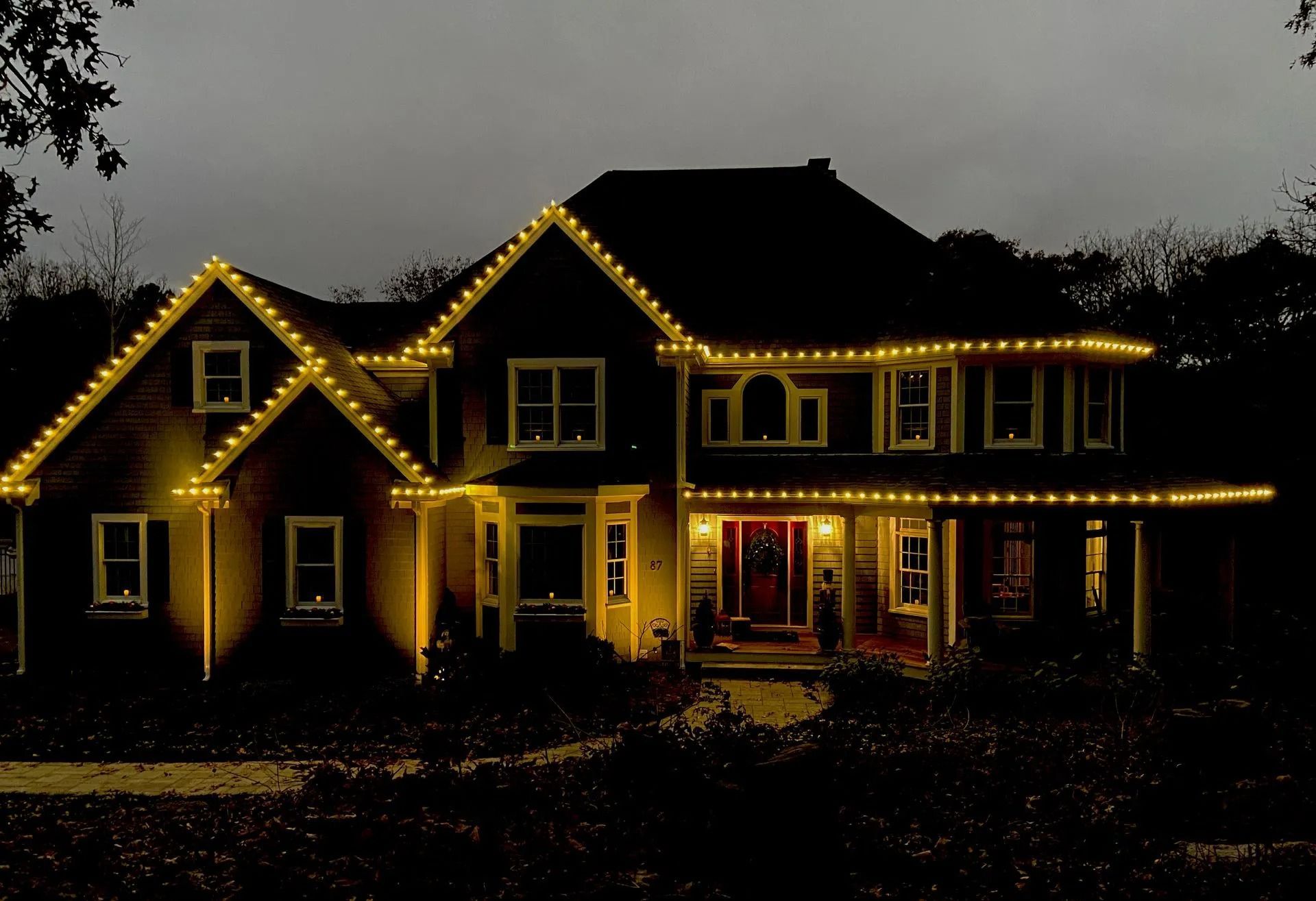 A two-story house at night, illuminated by yellow holiday lights outlining the roof and porch.