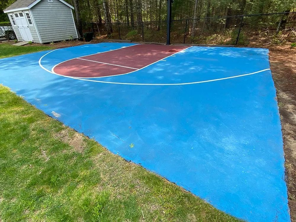 Blue and red basketball court in backyard, with hoop and small shed in the background.