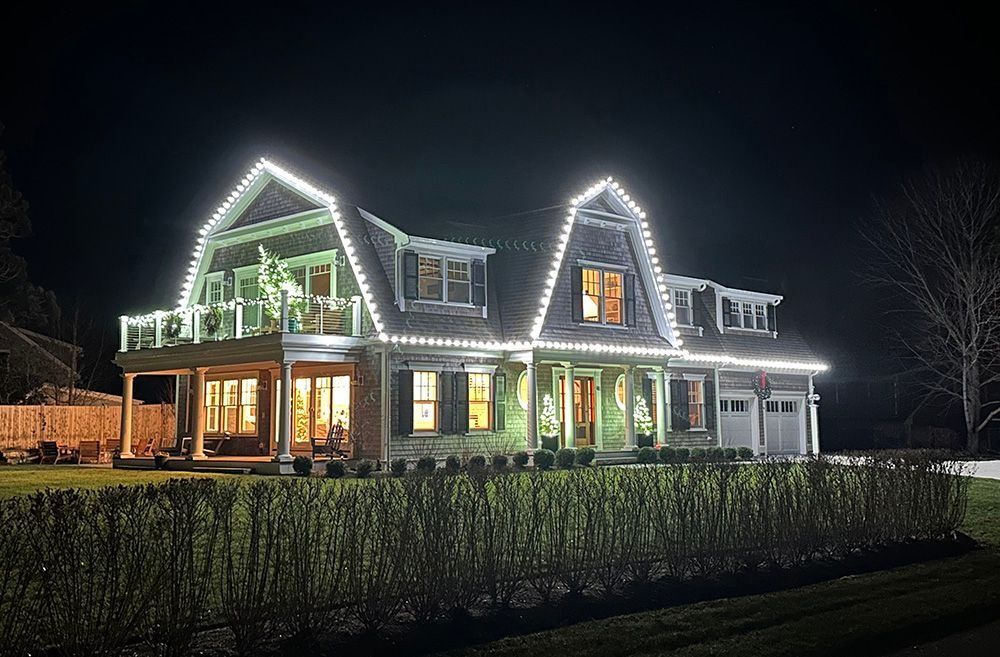 House at night, decorated with white lights along the roof and porch.