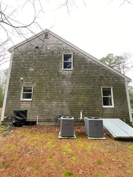 Side of a two-story house with weathered, moss-covered shingles, three windows, and two AC units.