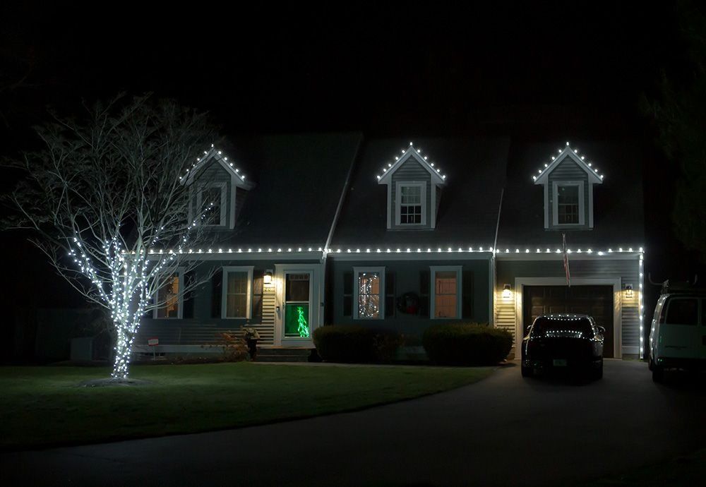 House decorated with white Christmas lights at night, with a tree also lit.