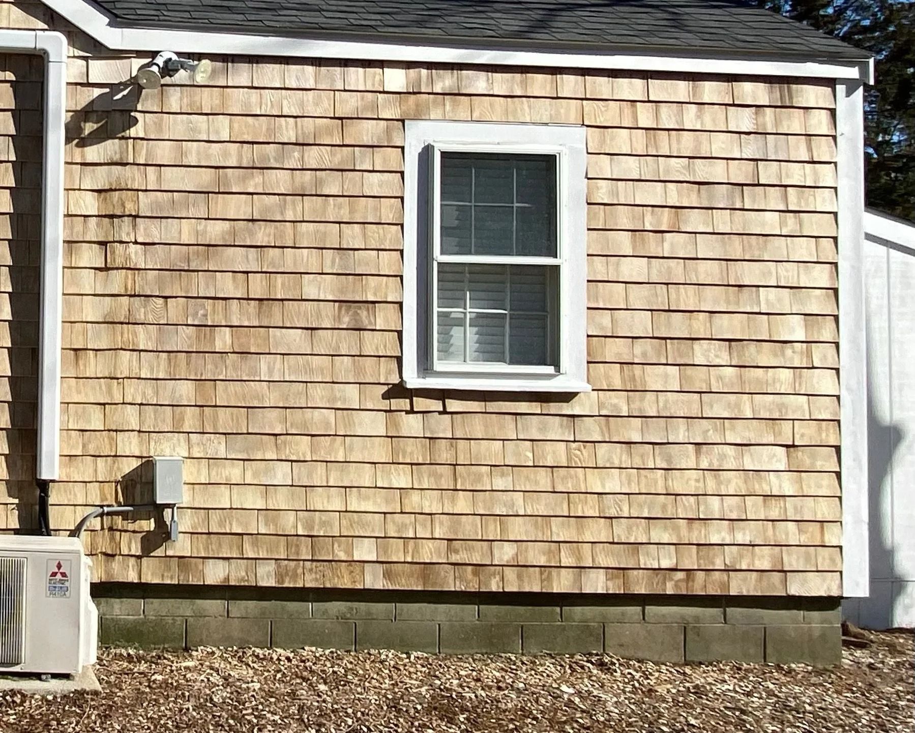 Exterior wall with weathered wooden shingles, a window, and an air conditioning unit.