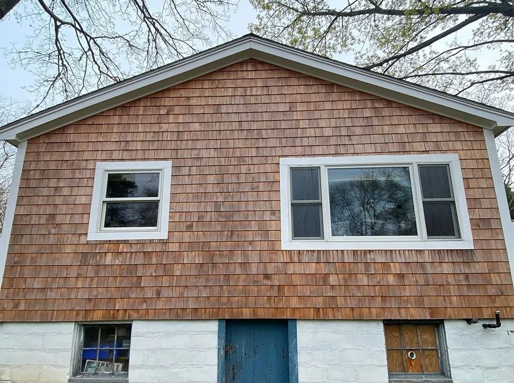 Building with cedar shingles, white-framed windows, and a blue door. The foundation is painted white.