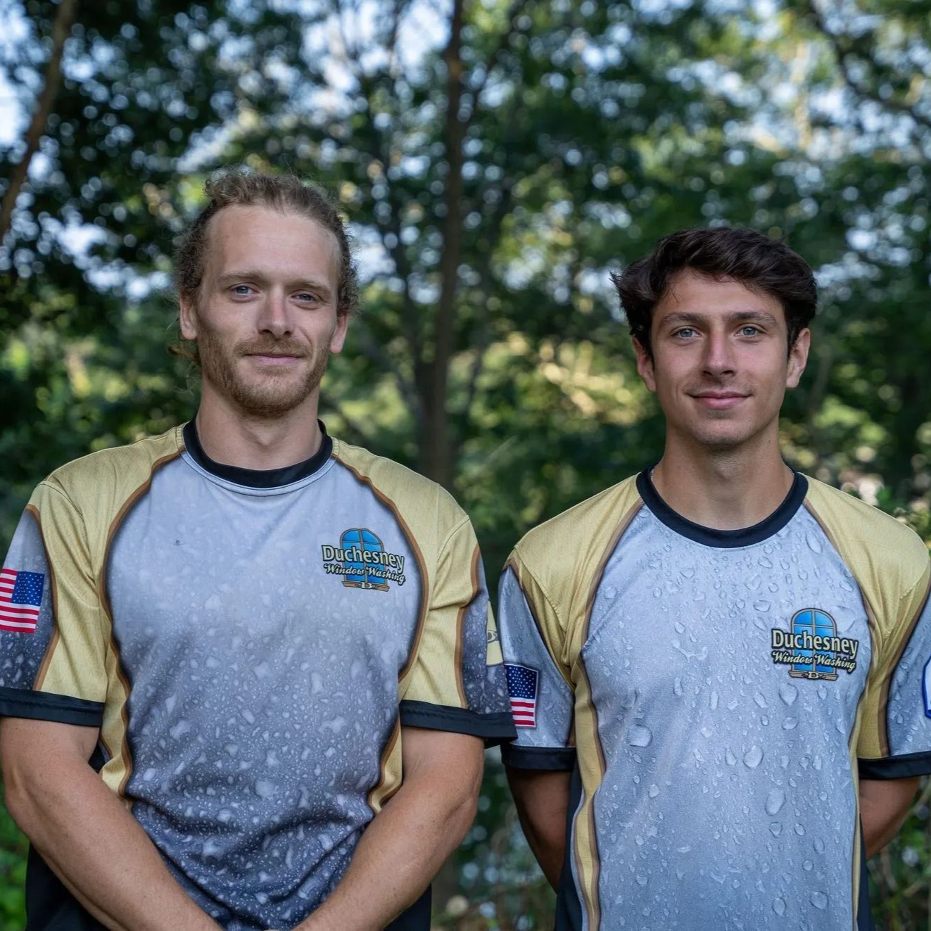 Two men in matching gold and gray athletic shirts pose outdoors.