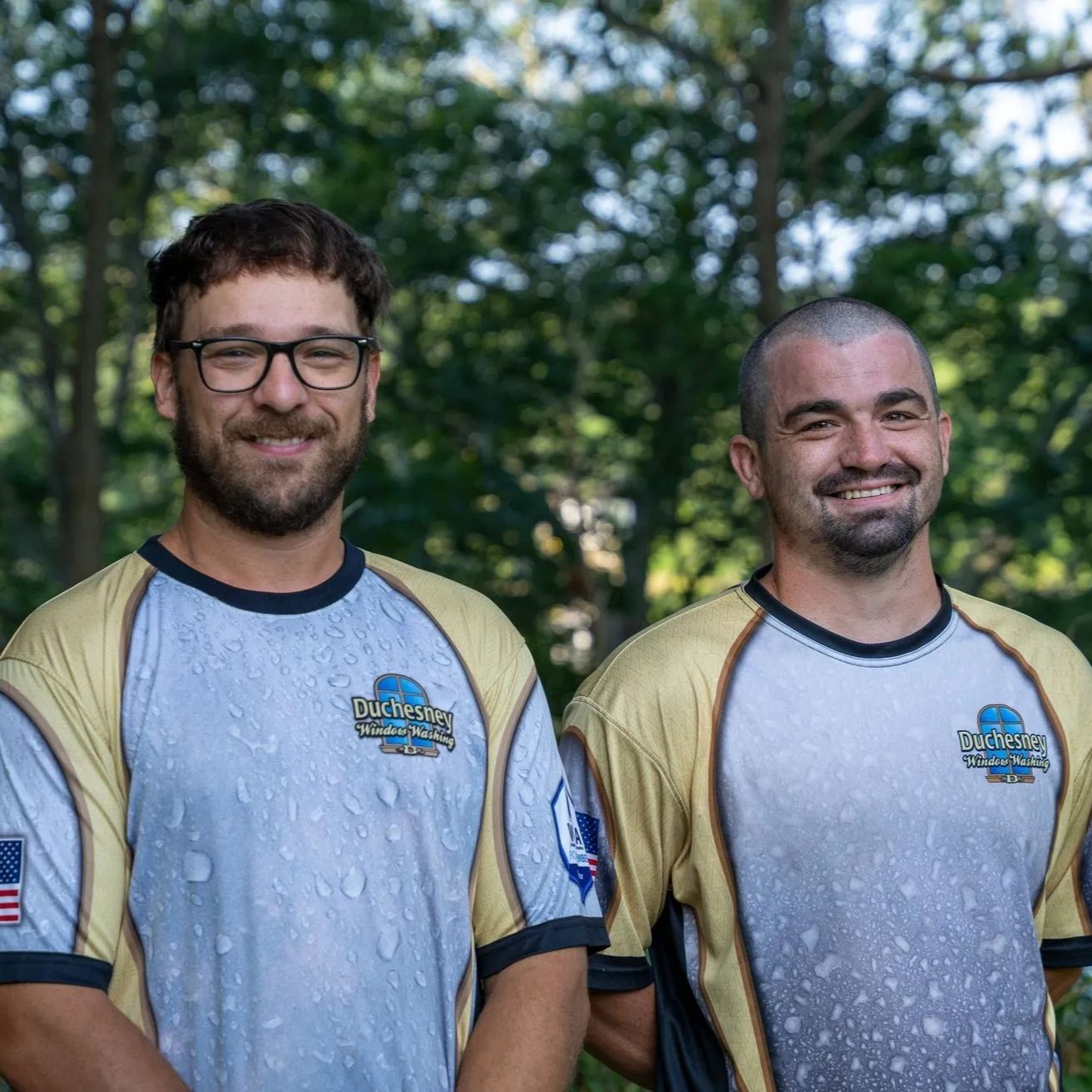 Two men in sports jerseys smiling in front of trees.