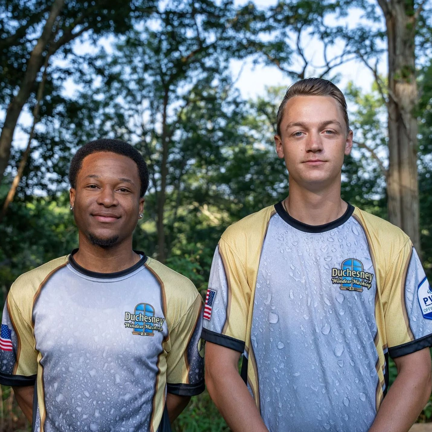 Two men in matching athletic shirts stand outdoors, smiling.