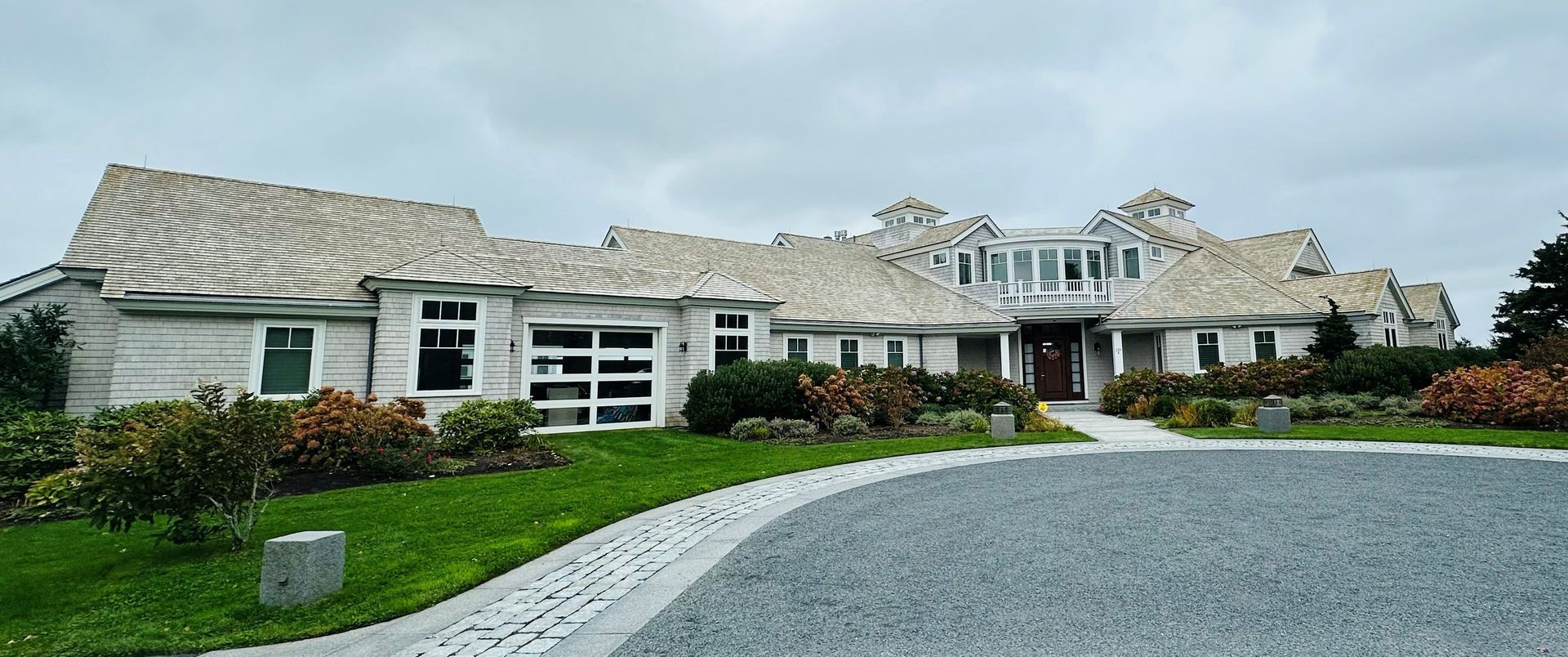 A large, light-colored house with a gravel driveway and green lawn under a cloudy sky.