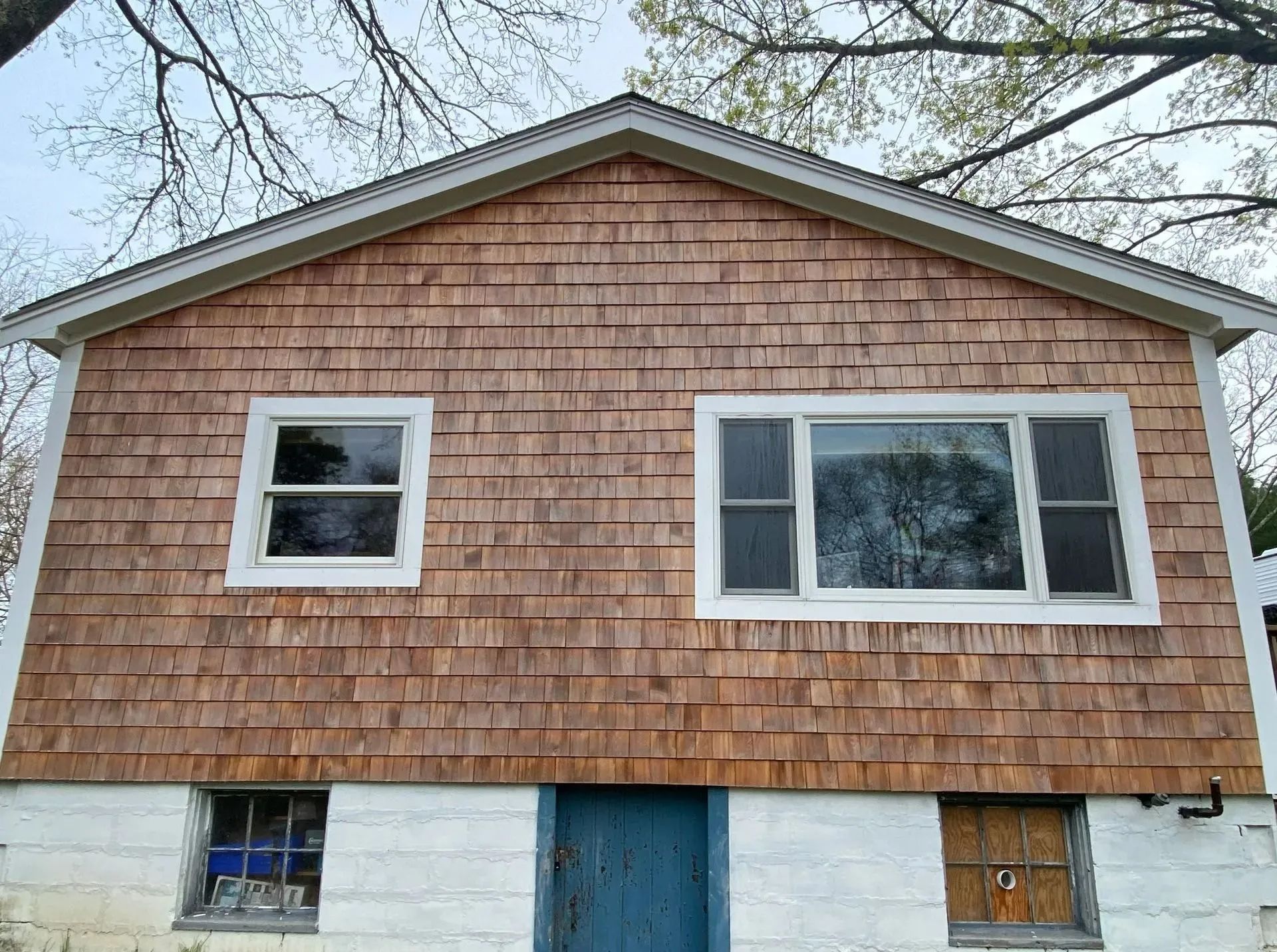 Cedar shingle siding on a house with white trim windows and a blue door.