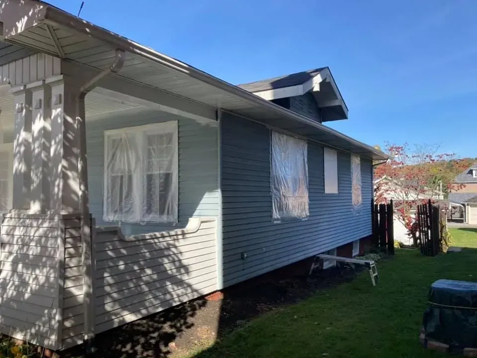 A house with blue siding and white trim is sitting on top of a lush green lawn.