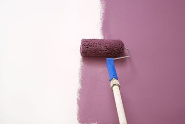 A paint roller is painting a wall purple.