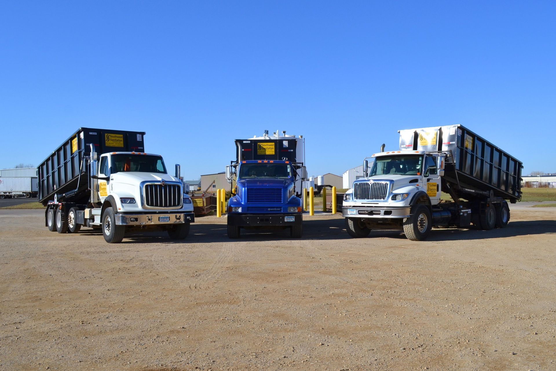 Black dumpster with yellow logos on a gravel lot near a white structure.