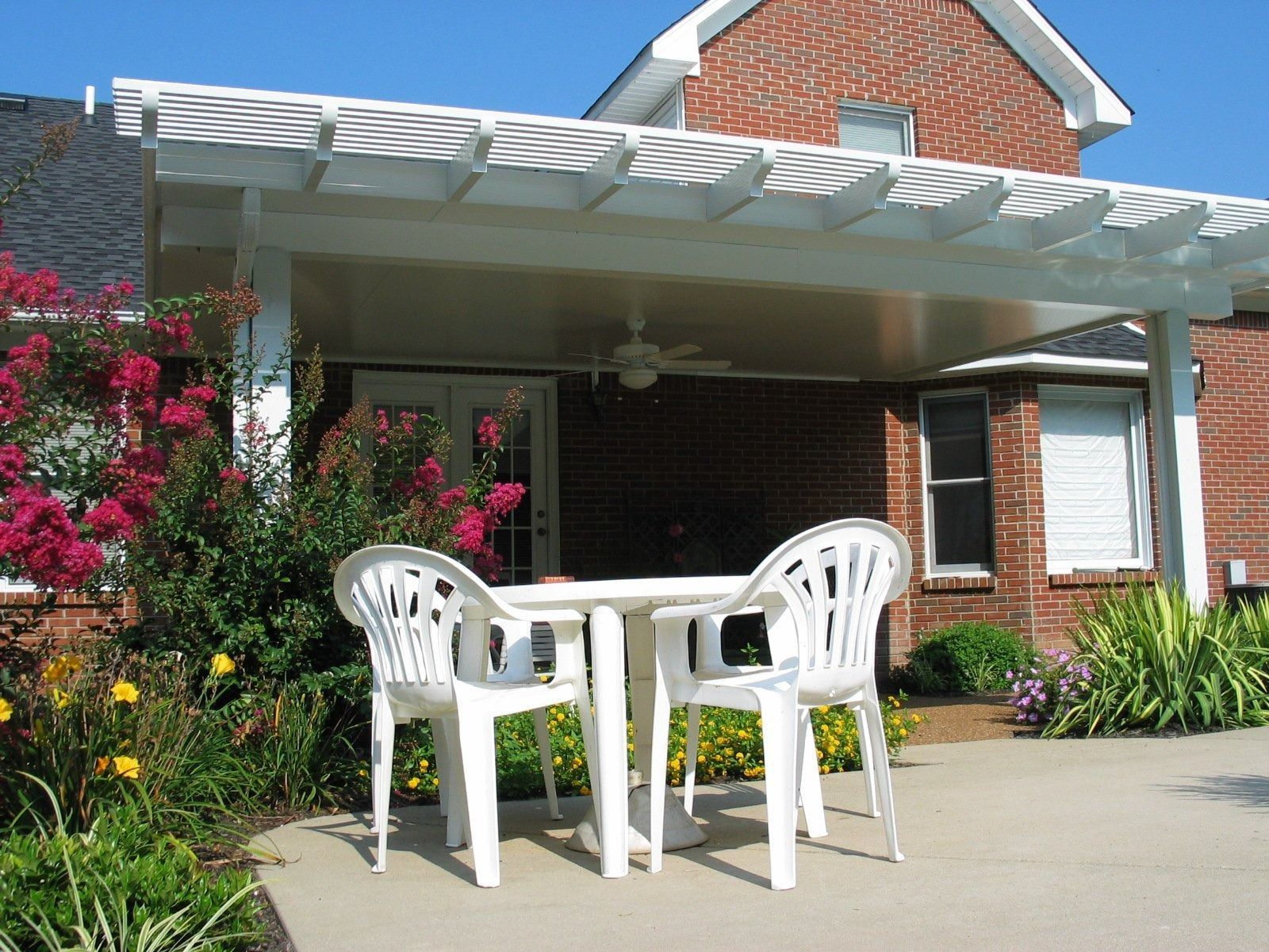 A table and chairs under a pergola in front of a brick house