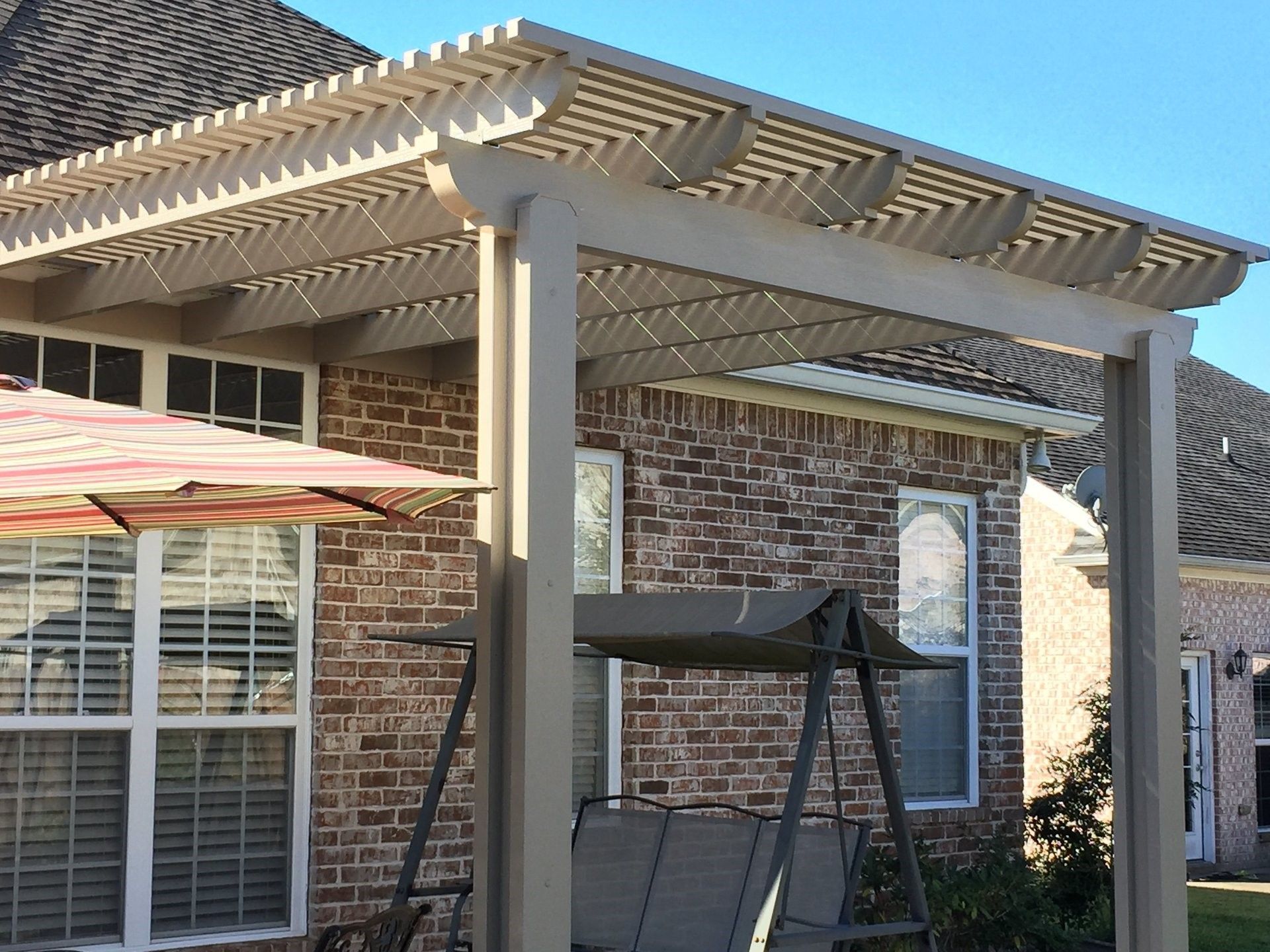 A brick house with a swing and umbrella under a pergola