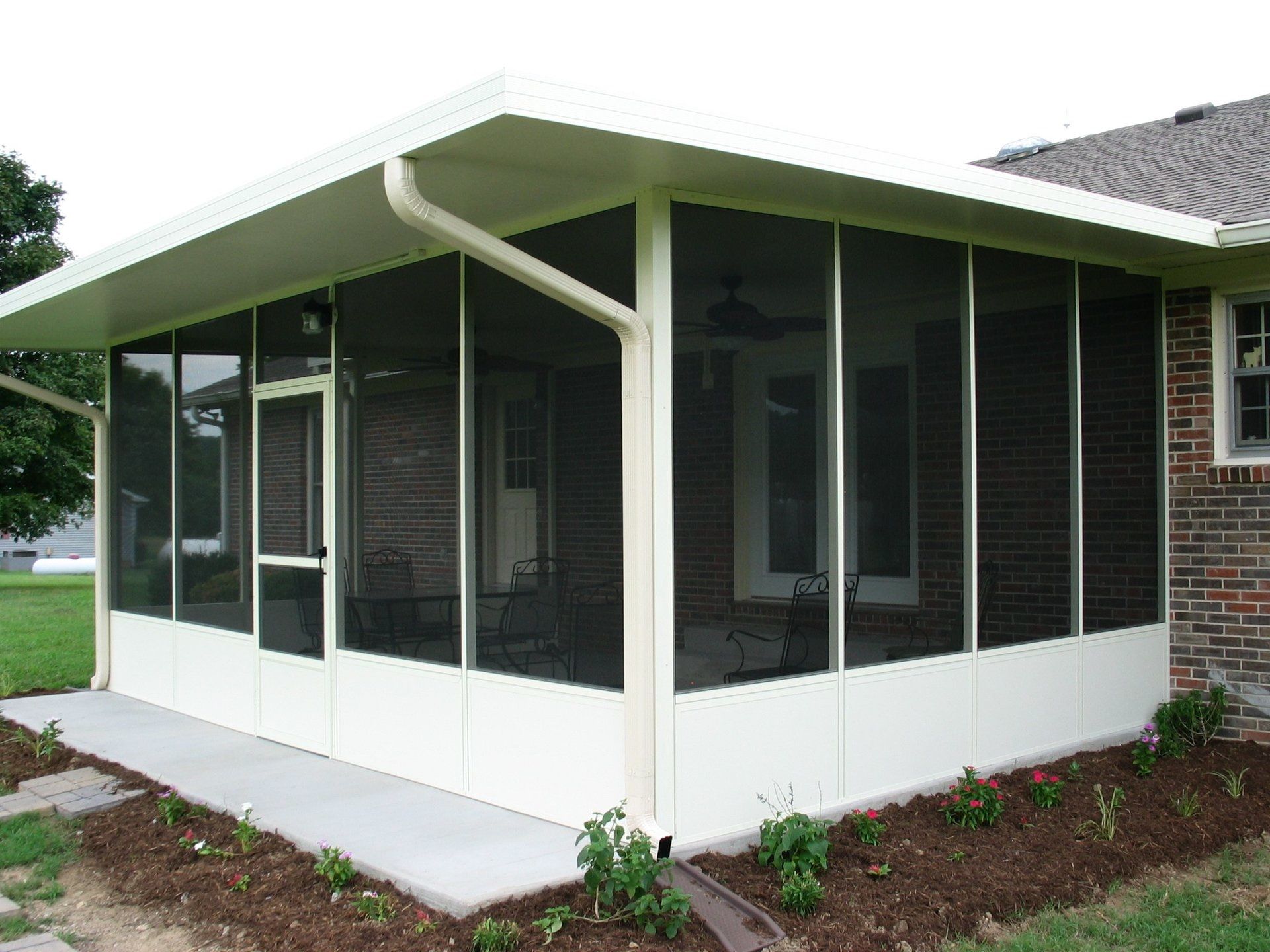 A screened in porch on the side of a brick house.