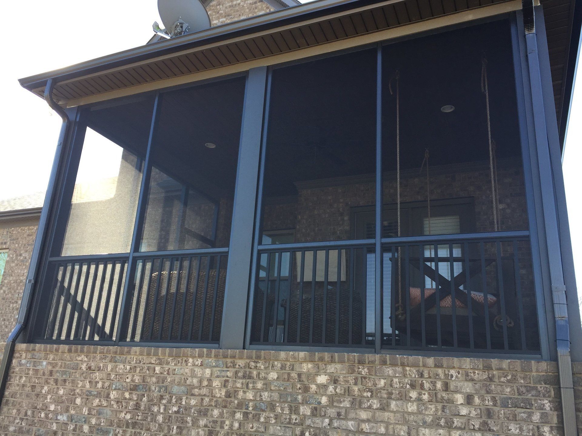 A screened in porch on the side of a brick house.