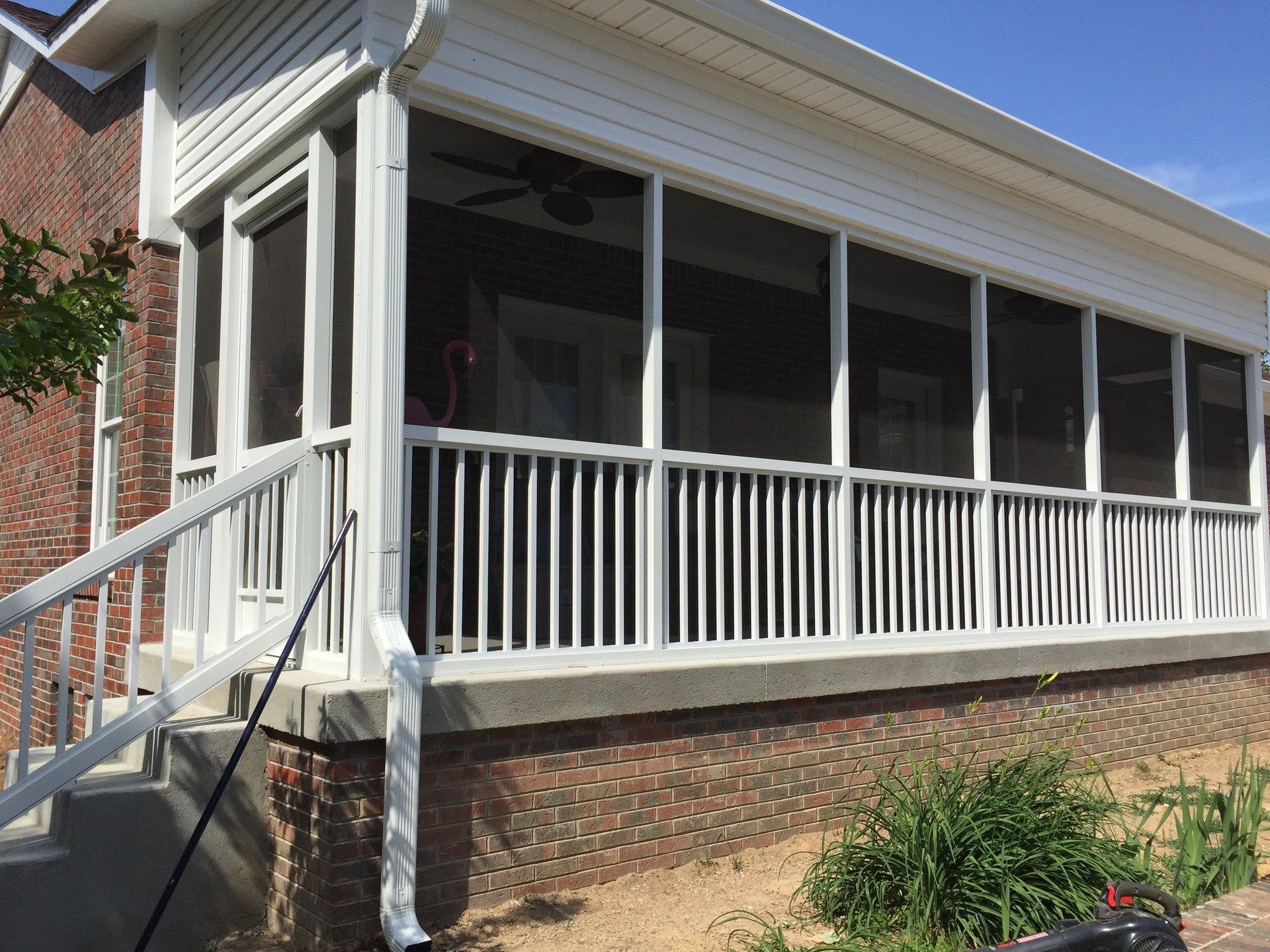 A screened in porch on the side of a brick house.