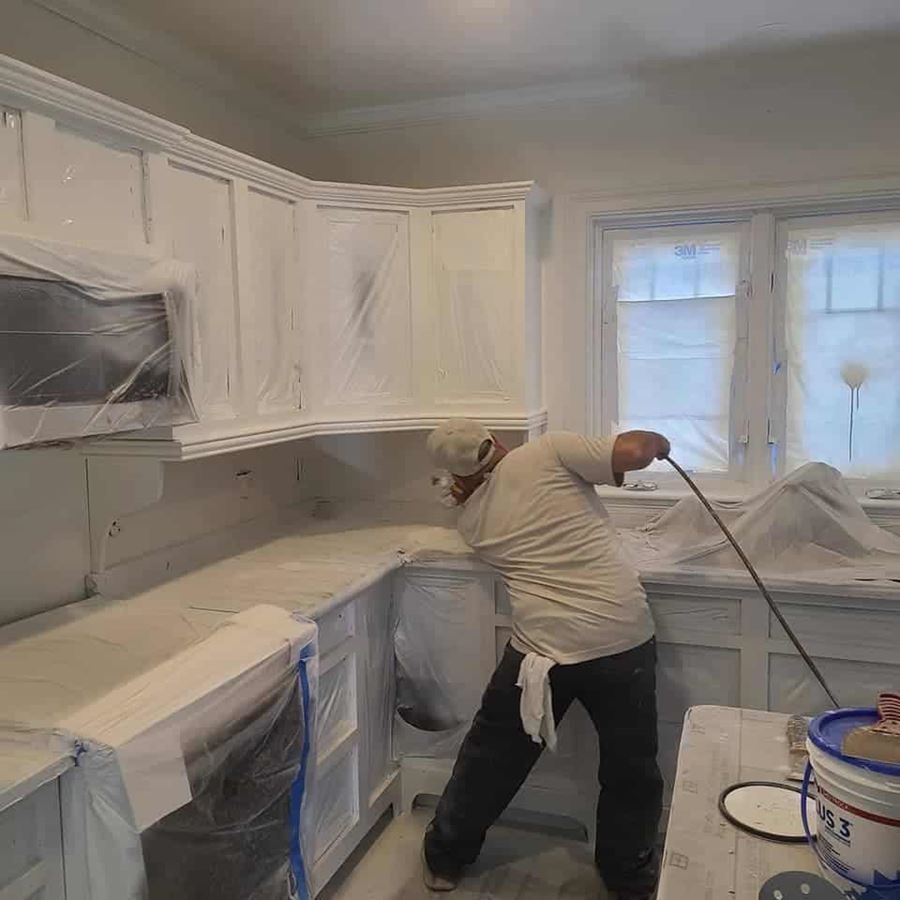 A man is painting a kitchen with white paint.
