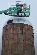 A man is standing in a bucket on top of a silo.