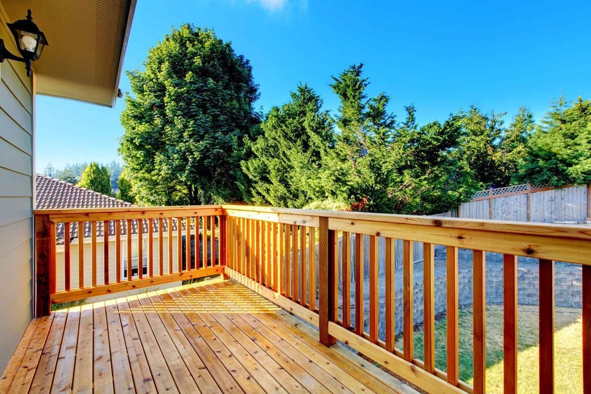 A wooden deck with a wooden railing and trees in the background.
