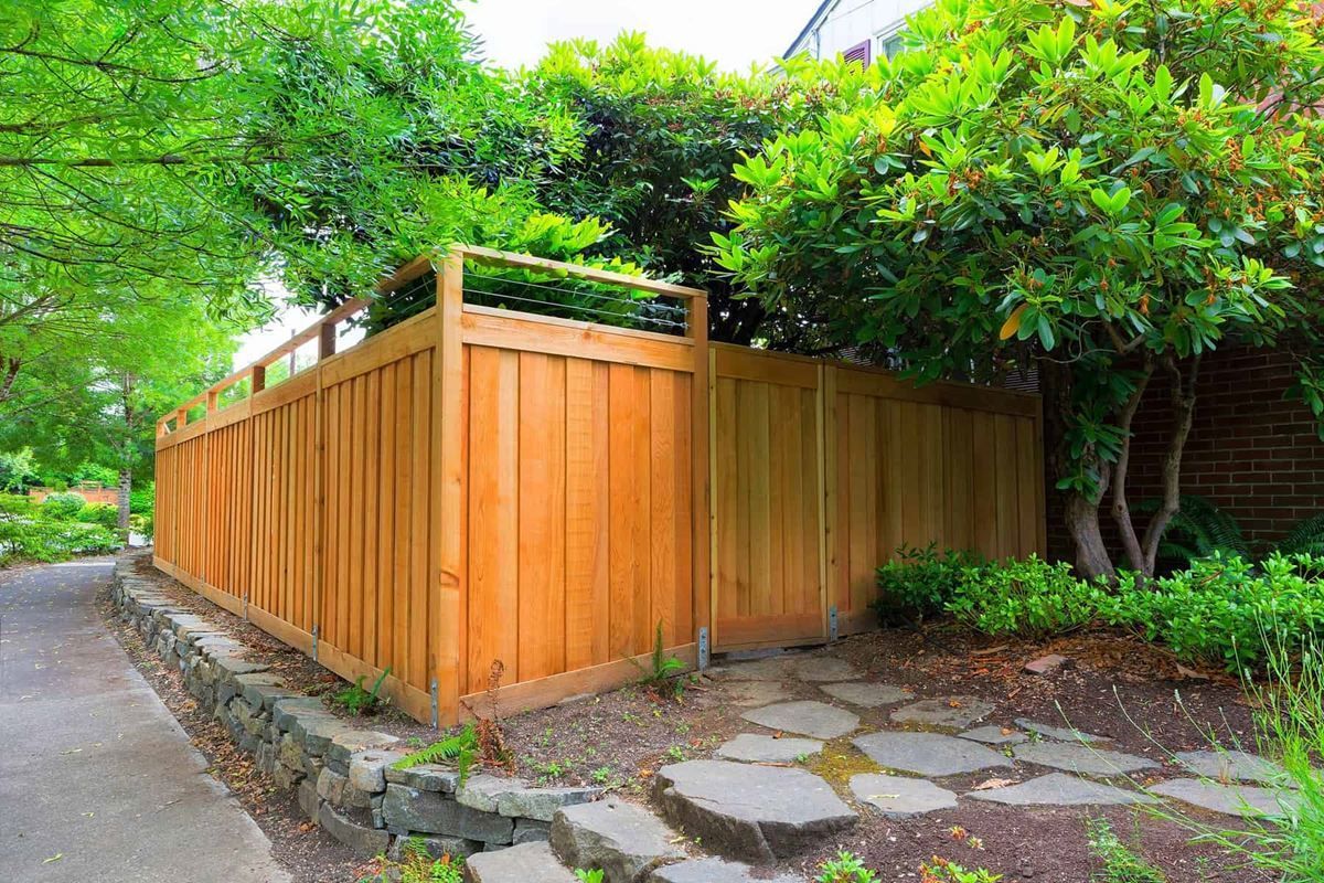 A wooden fence is surrounded by trees and a stone walkway.