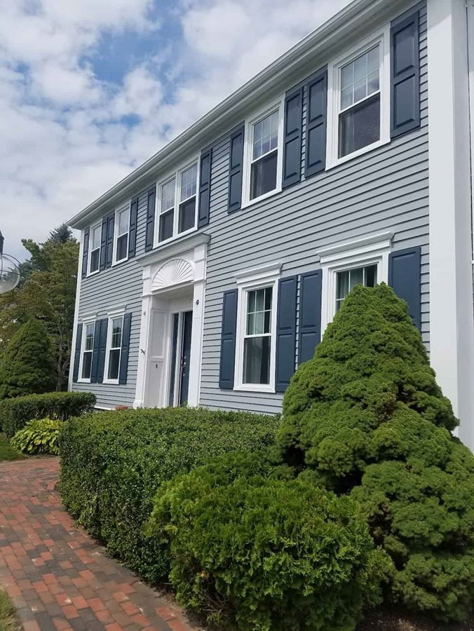A large house with blue shutters and a brick walkway leading to it.