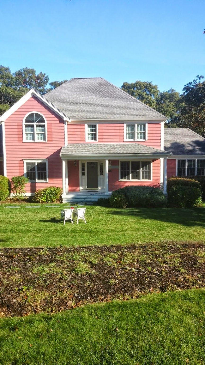 A large pink house with a gray roof and a large lawn in front of it.
