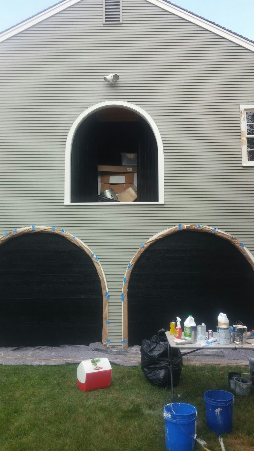 A house with three arched garage doors is being painted.