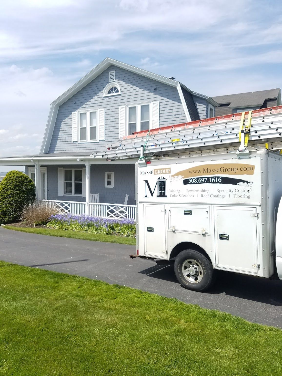 A white truck with a ladder on the back is parked in front of a house.