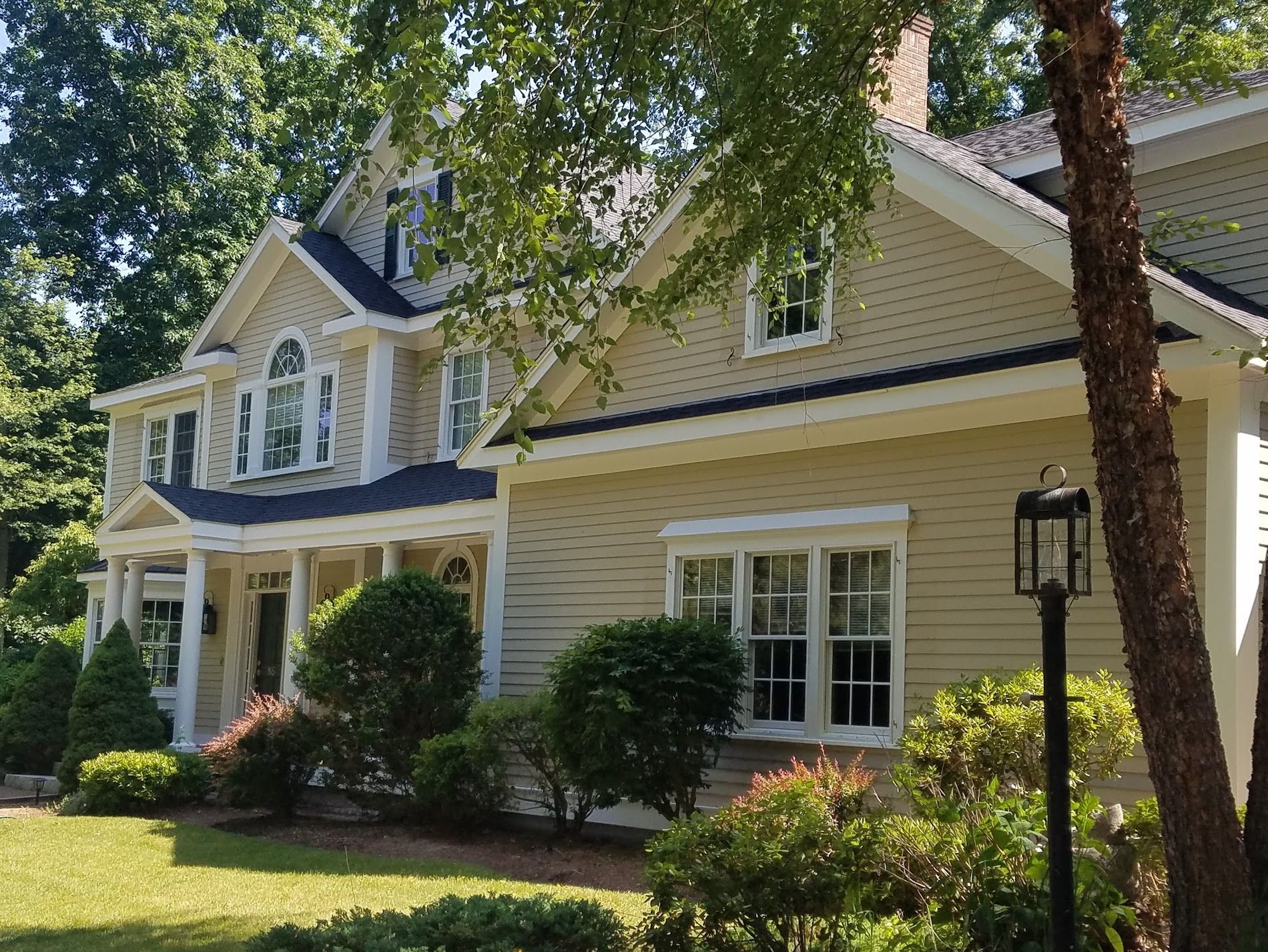 A large house with a blue roof is surrounded by trees and bushes.