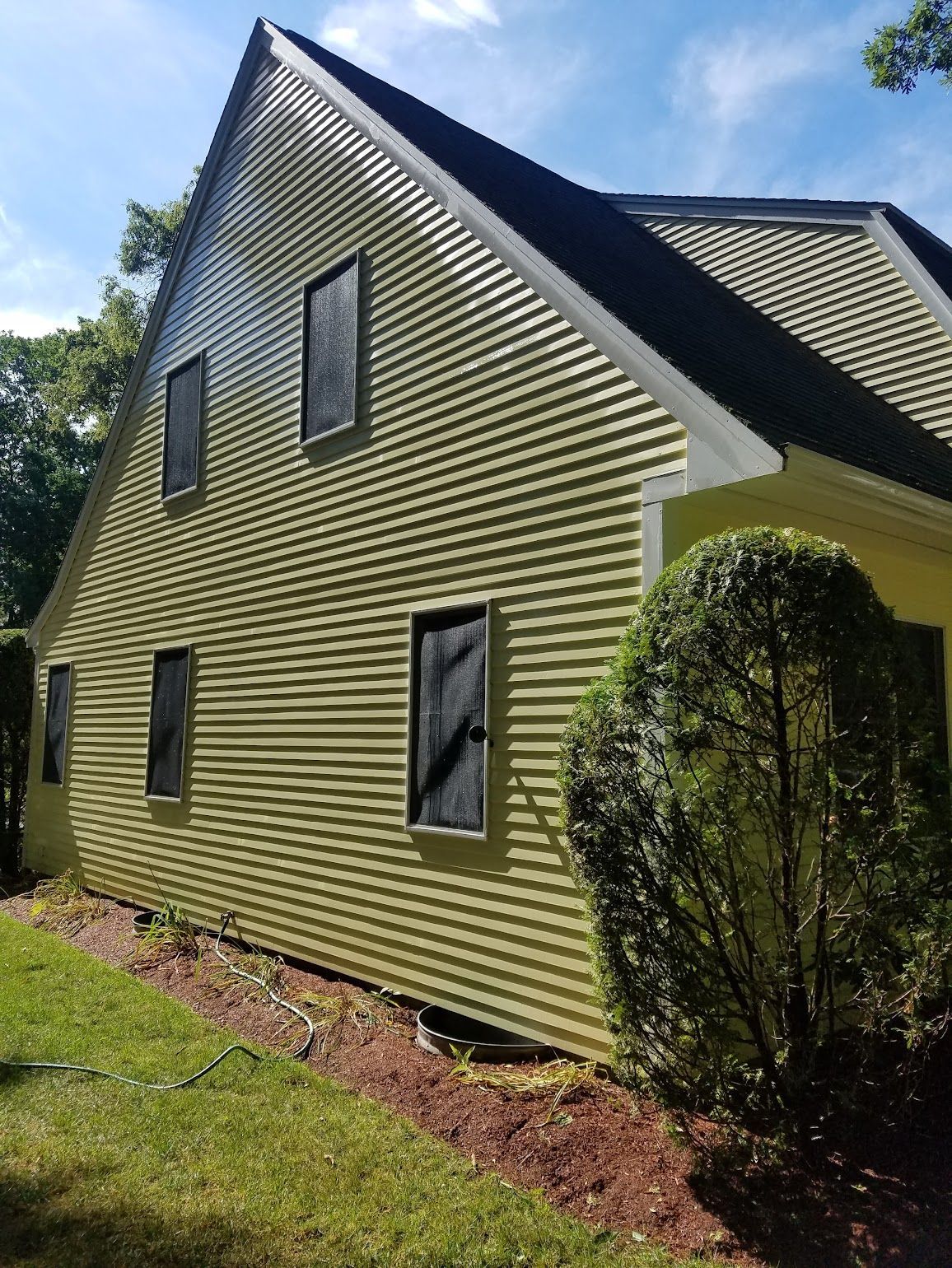 A yellow house with black windows and a black roof is sitting on top of a lush green field.