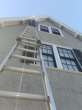 A man is standing on a ladder on the side of a house.