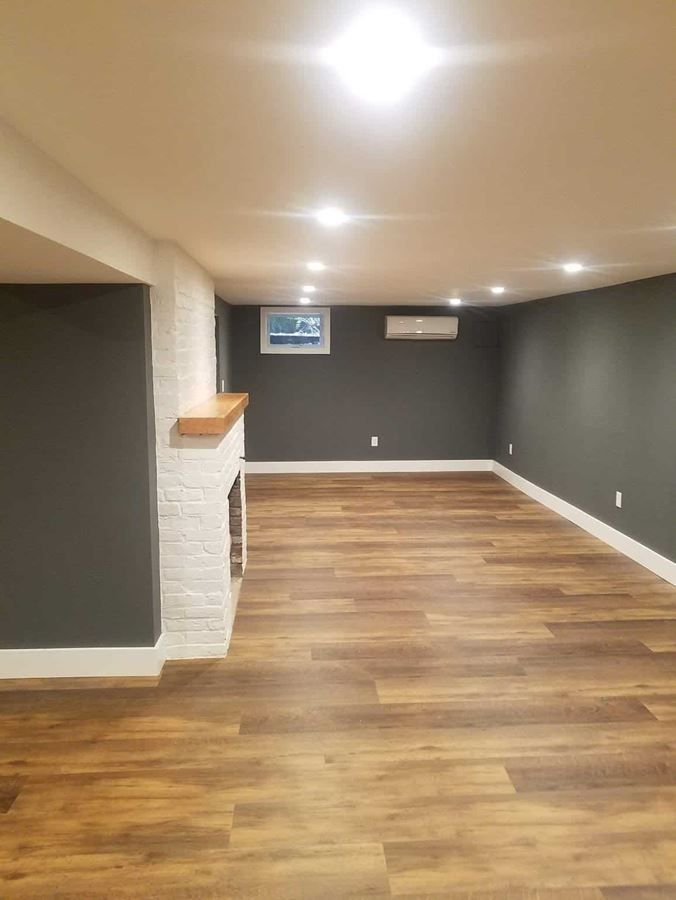 An empty basement with hardwood floors and a fireplace.