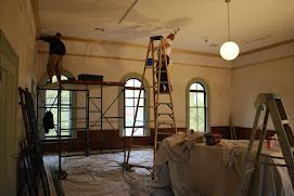 Two men are painting the ceiling of a room.