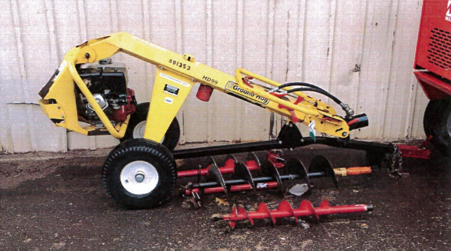 Yellow and black post hole digger with augers on pavement.