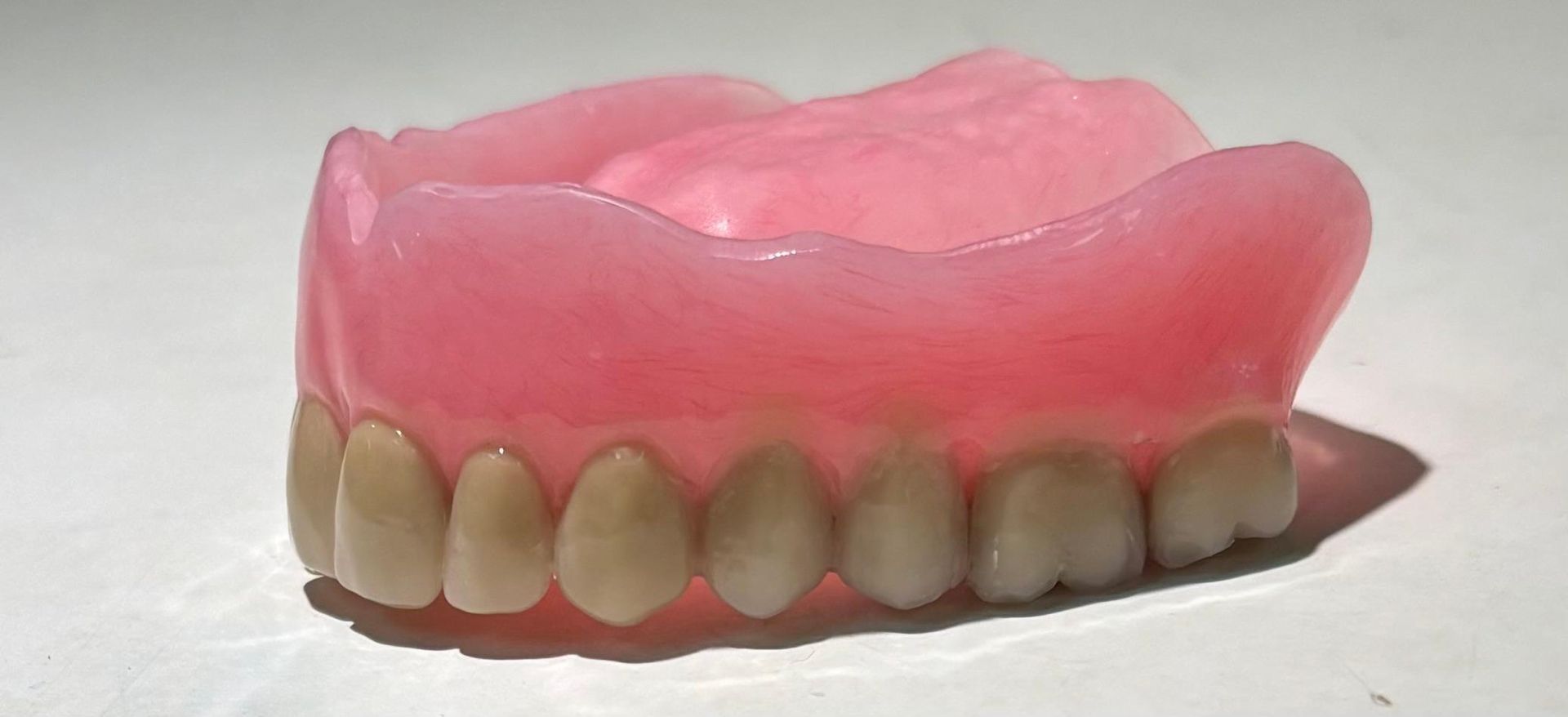 A complete set of upper Hypoallergenic dentures with pink acrylic gums and white teeth against a plain white background.